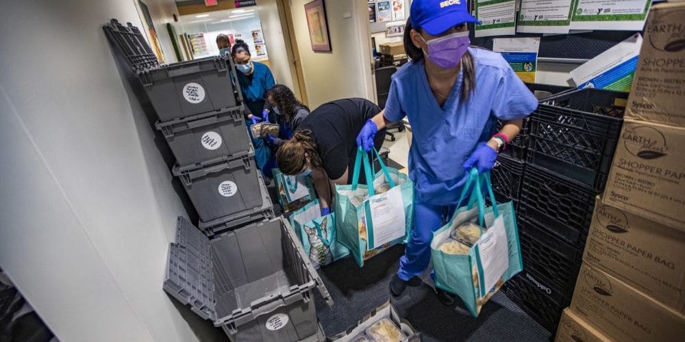 AmeriCorps service member Paloma Suarez carries bags of frozen meals to the entryway of South End Community Health Center for families to pick up. (Jesse Costa/WBUR)