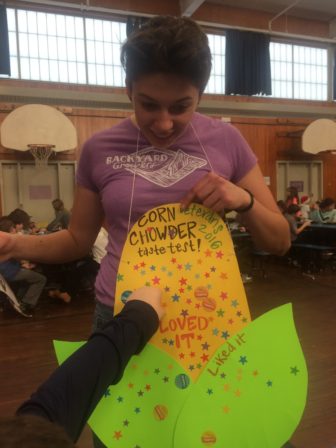 Amy holds up poster shaped like corn so kids can vote on whether they liked the corn chowder