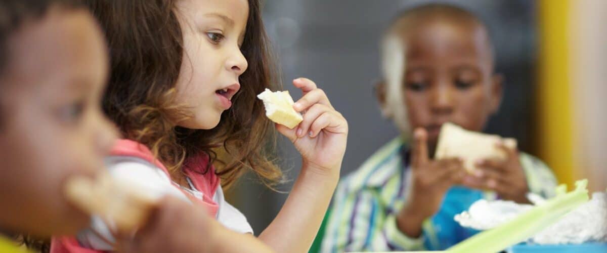 3 children of color sitting in a cafeteria eating lunch