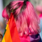 A person with pink hair holds a rainbow flag