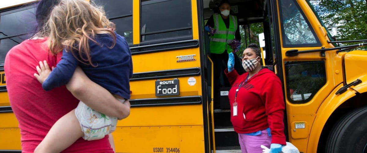 school nutrition staff talking with a parent in front of the open door of a school bus