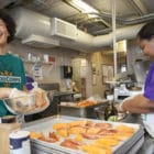 A FoodCorps service member and cafeteria staffer working together in a school kitchen