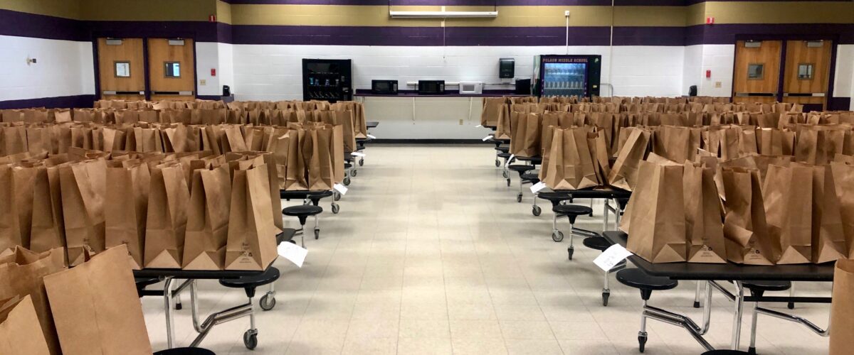 Rows of tables hold paper bags filled with food items