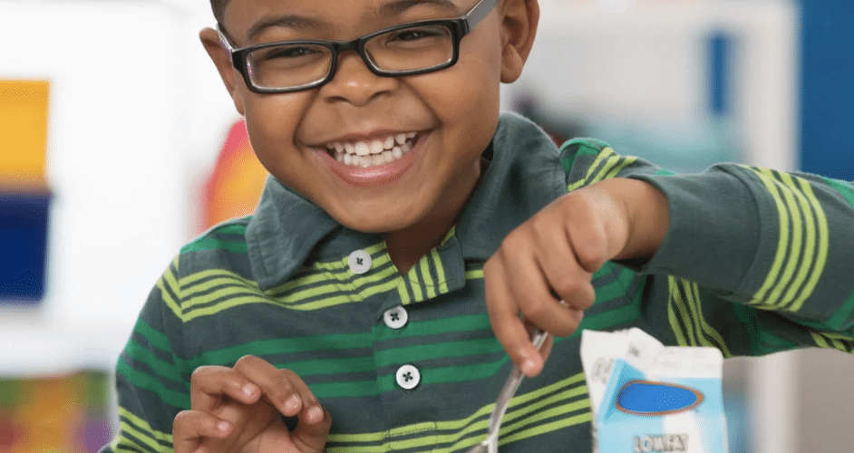 small child smiling while digging in to food on a school lunch tray