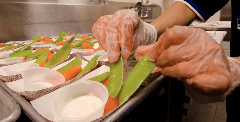 School nutrition staff placing snap peas and carrots onto lunch trays.