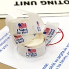 A roll of I Voted stickers atop voting paperwork